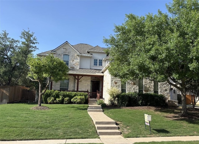 traditional-style home featuring stucco siding, stone siding, a front yard, and fence