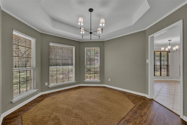 unfurnished dining area featuring a raised ceiling, a chandelier, a wealth of natural light, and wood finished floors