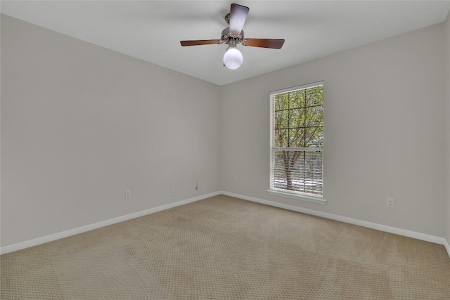 empty room featuring light colored carpet, a ceiling fan, and baseboards
