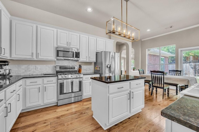 kitchen with arched walkways, crown molding, white cabinetry, and stainless steel appliances