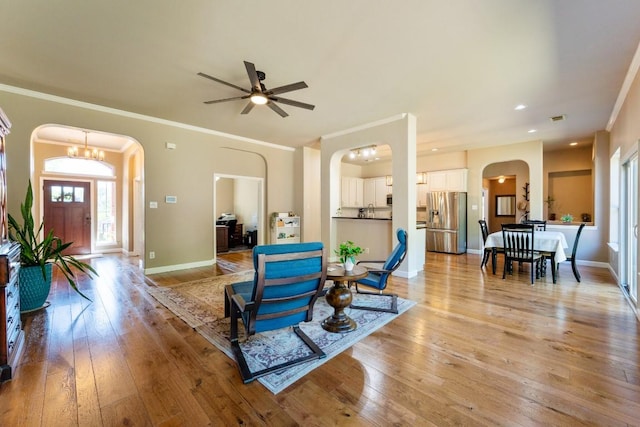 living area with ornamental molding, light wood-style flooring, a ceiling fan, and arched walkways