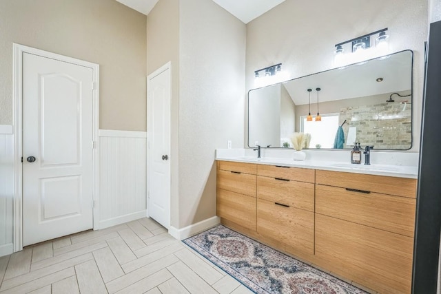 bathroom with tiled shower, double vanity, and a sink