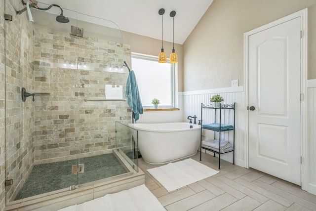 bathroom featuring a shower stall, a soaking tub, wainscoting, and lofted ceiling