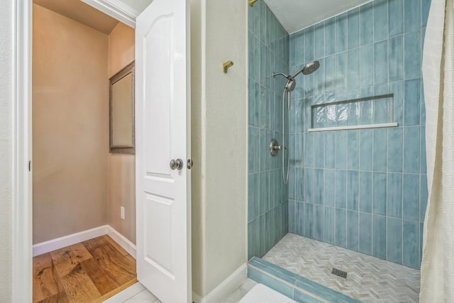 bathroom featuring tiled shower, wood finished floors, and baseboards