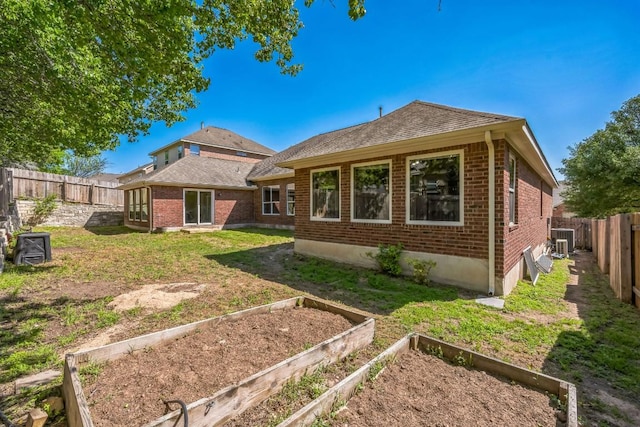 rear view of property featuring brick siding, a garden, a fenced backyard, and a yard