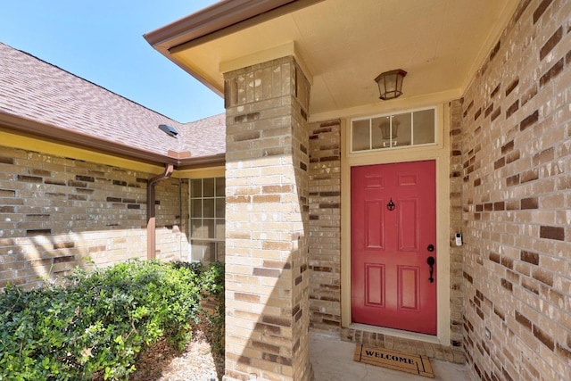 doorway to property featuring roof with shingles and brick siding