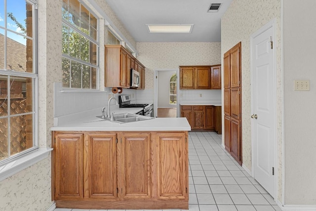 kitchen with wallpapered walls, a peninsula, visible vents, stainless steel appliances, and a sink
