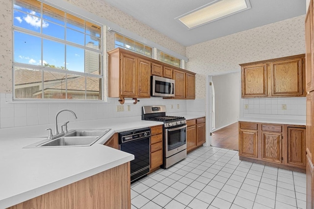 kitchen with appliances with stainless steel finishes, a sink, wallpapered walls, and a healthy amount of sunlight