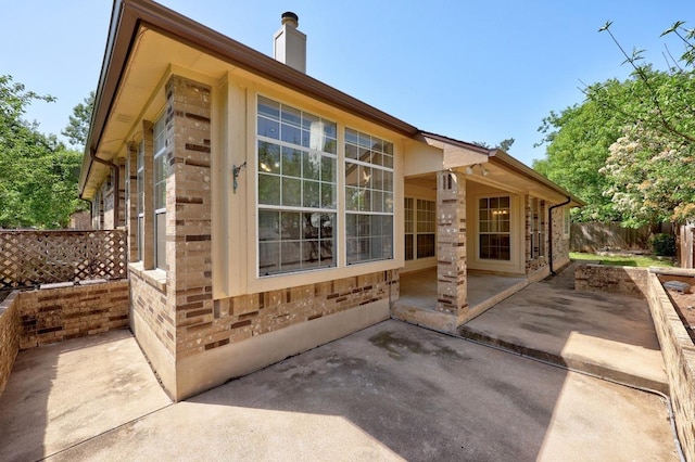 view of side of home with brick siding, fence, a patio, and a chimney