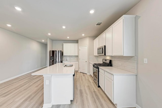 1528 Longhorn Ranch Dr, Leander, TX 78641 - kitchen featuring appliances with stainless steel finishes, tasteful backsplash, light wood finished floors, an island with sink, and white cabinets