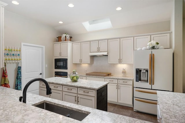 109 Lombardia Dr, Lakeway, TX 78734 - kitchen with black appliances, a skylight, under cabinet range hood, decorative backsplash, and light stone counters