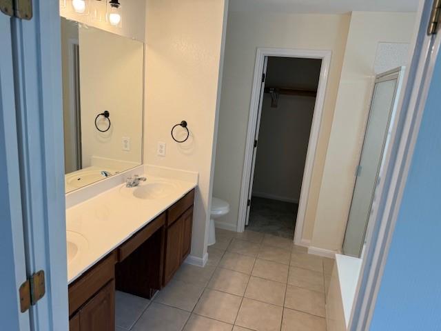 161 Carriage Way, Kyle, TX 78640 - bathroom with double vanity, a walk in closet, tile patterned floors, and a shower with door