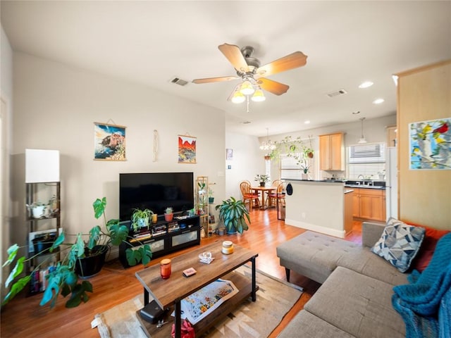 living area featuring light wood-style floors, ceiling fan with notable chandelier, and visible vents