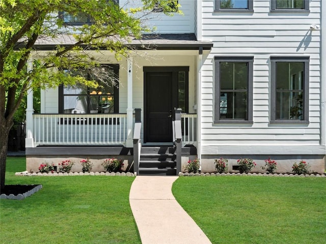 view of exterior entry featuring covered porch and a lawn