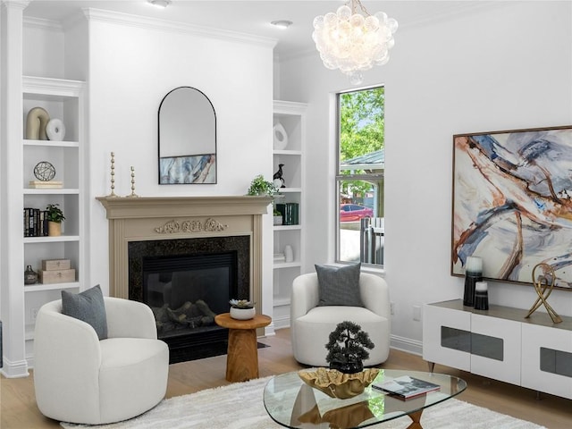 living room with built in features, an inviting chandelier, ornamental molding, wood finished floors, and a high end fireplace