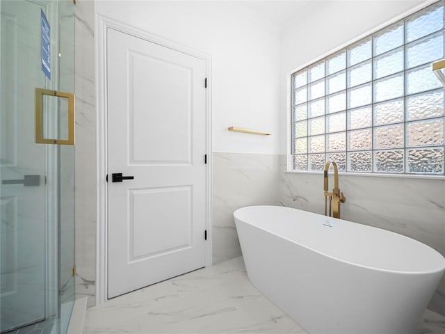 full bathroom with tile walls, marble finish floor, a freestanding tub, and wainscoting