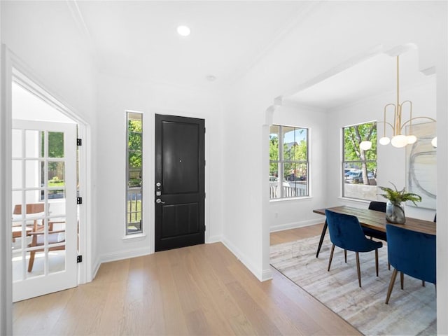 foyer featuring a chandelier, light wood finished floors, baseboards, and ornamental molding