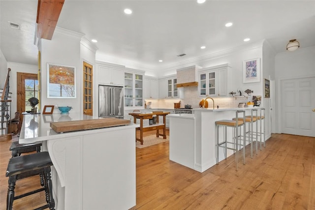 kitchen featuring a peninsula, crown molding, visible vents, a breakfast bar area, and high end refrigerator