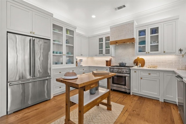 kitchen with custom range hood, light countertops, crown molding, visible vents, and premium appliances