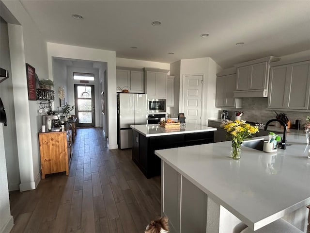 145 Cyrus Milton Dr, Buda, TX 78610 - kitchen featuring appliances with stainless steel finishes, a kitchen island, light countertops, dark wood-style floors, and tasteful backsplash