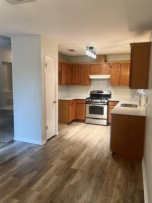 506 Clearcreek Dr, Leander, TX 78641 - kitchen with gas range, a sink, under cabinet range hood, dark wood-style flooring, and brown cabinets