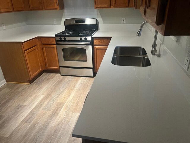 506 Clearcreek Dr, Leander, TX 78641 - kitchen featuring gas range, a sink, brown cabinetry, light wood-style flooring, and light countertops