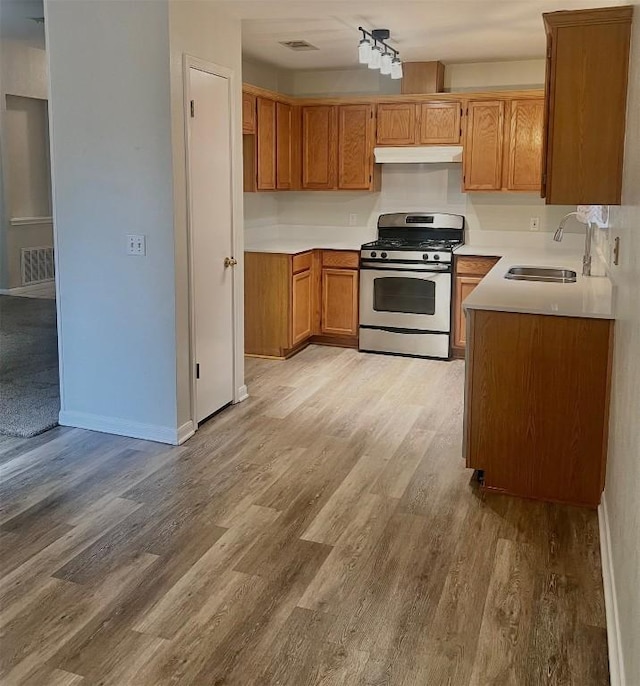 506 Clearcreek Dr, Leander, TX 78641 - kitchen featuring gas stove, a sink, under cabinet range hood, light wood finished floors, and brown cabinetry