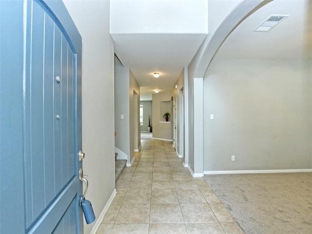 foyer featuring visible vents, light carpet, arched walkways, light tile patterned floors, and baseboards