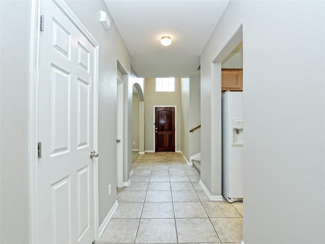 hall featuring arched walkways, stairs, baseboards, and light tile patterned floors