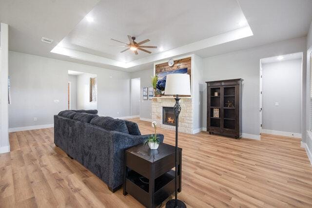 3401 Bandit Ct, Kempner, TX 76539 - living area with a tray ceiling, a ceiling fan, a stone fireplace, and light wood-style flooring