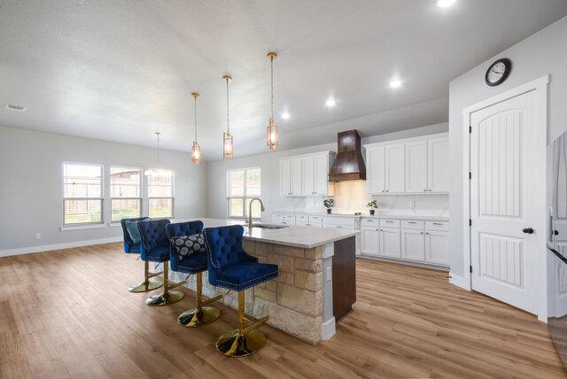 3401 Bandit Ct, Kempner, TX 76539 - kitchen featuring custom range hood, a breakfast bar, light wood-style floors, white cabinets, and a kitchen island with sink