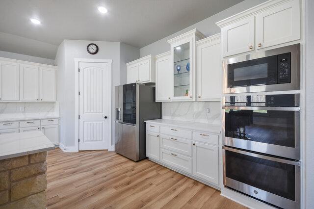 3401 Bandit Ct, Kempner, TX 76539 - kitchen with stainless steel appliances, white cabinets, light wood-style flooring, backsplash, and recessed lighting