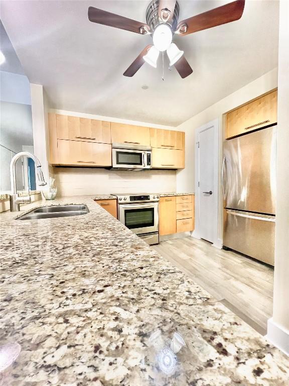 603 Davis St Unit 804, Austin, TX 78701 - kitchen with appliances with stainless steel finishes, light brown cabinets, a sink, light stone counters, and light wood-style floors