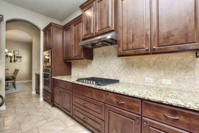 1706 Ambling Trl, Cedar Park, TX 78613 - kitchen with under cabinet range hood, stainless steel appliances, arched walkways, backsplash, and light stone countertops