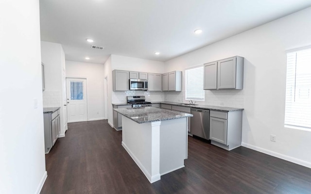 108 Biscayne Dr, Hutto, TX 78634 - kitchen featuring stainless steel appliances, dark wood finished floors, backsplash, gray cabinetry, and a kitchen island