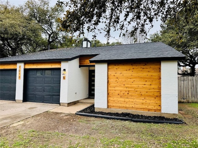 view of front of property featuring a shingled roof, an attached garage, fence, brick siding, and driveway