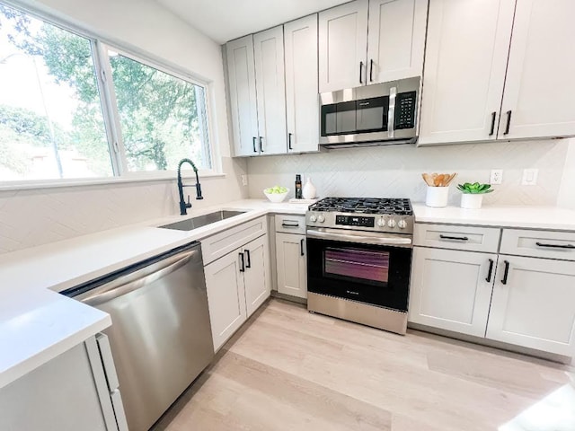 kitchen with decorative backsplash, appliances with stainless steel finishes, a sink, light countertops, and light wood finished floors