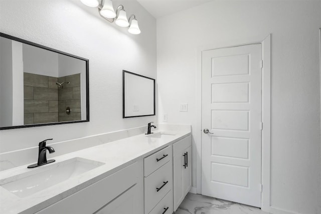 full bath featuring marble finish flooring, tiled shower, and double vanity