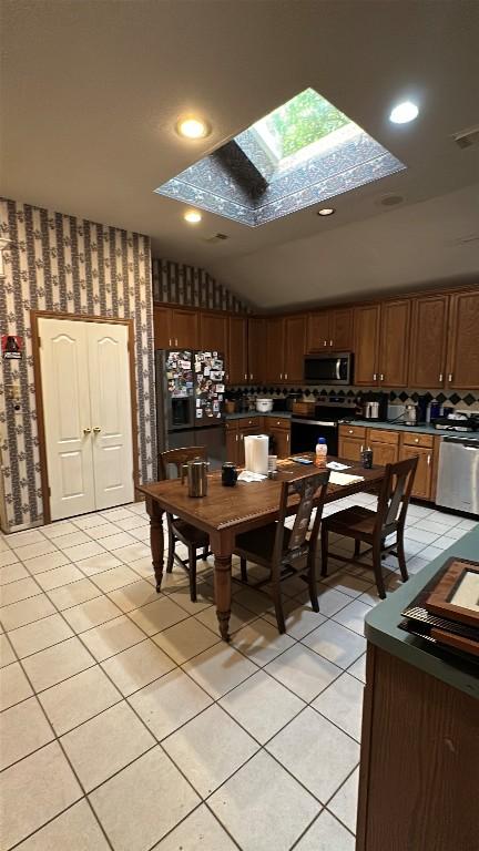 dining area featuring visible vents, vaulted ceiling with skylight, light tile patterned floors, and wallpapered walls