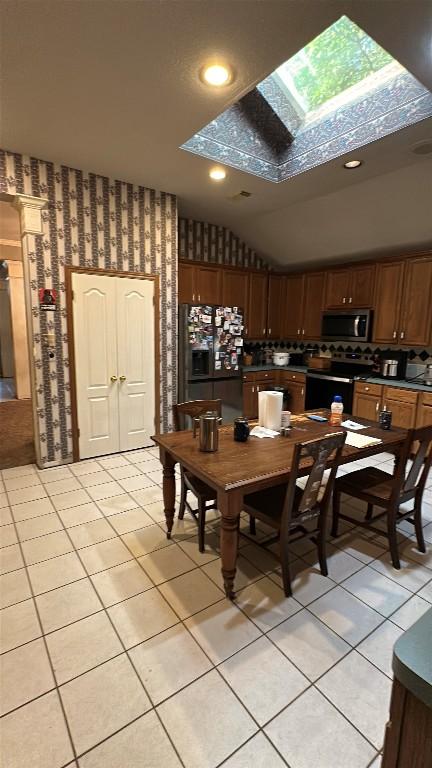 dining room featuring light tile patterned floors, wallpapered walls, and lofted ceiling with skylight