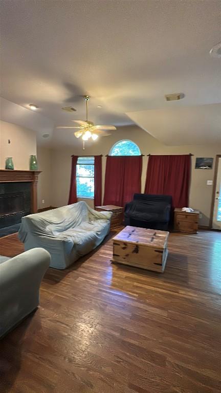 living room featuring dark wood-style flooring, a ceiling fan, vaulted ceiling, and a fireplace