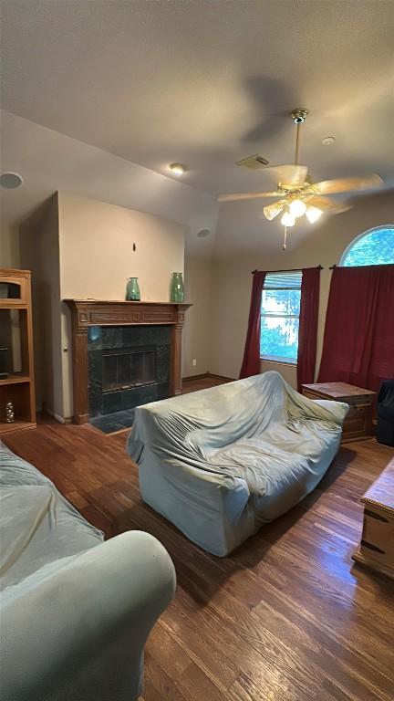 living area featuring a tiled fireplace, visible vents, a ceiling fan, and wood finished floors