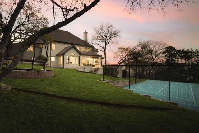 2809 Waterbank Cv, Austin, TX 78746 - back of house at dusk featuring a yard, basketball court, stucco siding, and a chimney