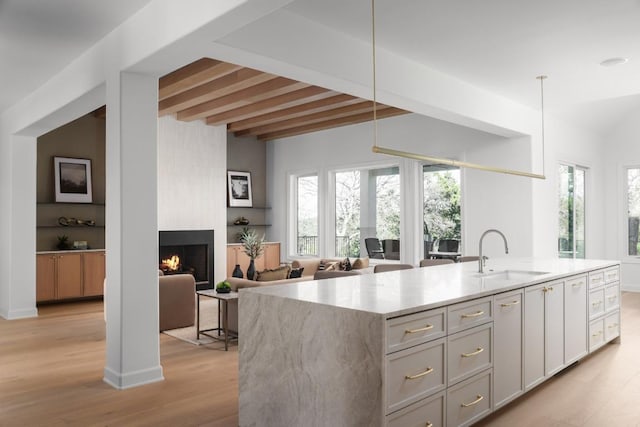 2809 Waterbank Cv, Austin, TX 78746 - kitchen with light wood-type flooring, a fireplace, an island with sink, decorative light fixtures, and light stone counters
