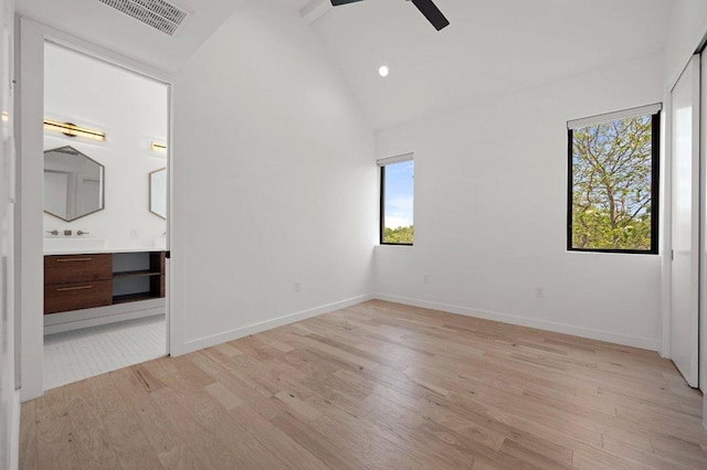 unfurnished bedroom featuring visible vents, connected bathroom, light wood-style flooring, and vaulted ceiling