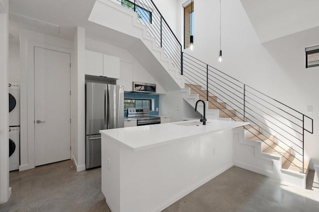 kitchen featuring a peninsula, concrete flooring, white cabinetry, a sink, and appliances with stainless steel finishes