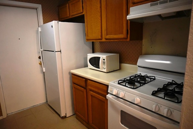 817 Lexington Rd, Elgin, TX 78621 - kitchen with light countertops, white appliances, under cabinet range hood, brown cabinetry, and wallpapered walls