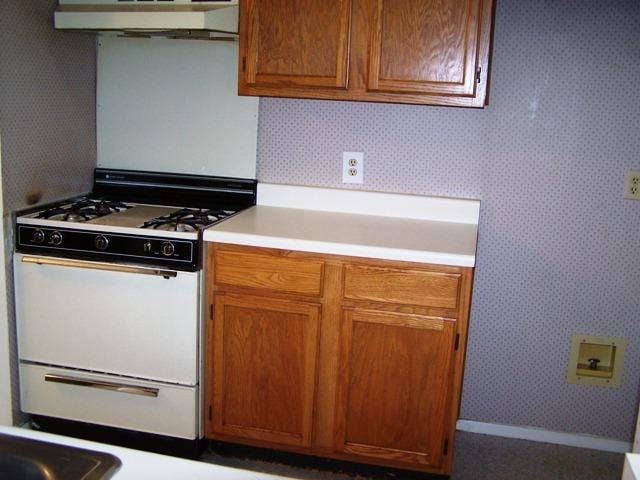 817 Lexington Rd, Elgin, TX 78621 - kitchen featuring light countertops, under cabinet range hood, white range with gas cooktop, brown cabinetry, and wallpapered walls