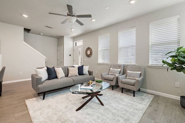 living room with baseboards, visible vents, wood finished floors, and a ceiling fan
