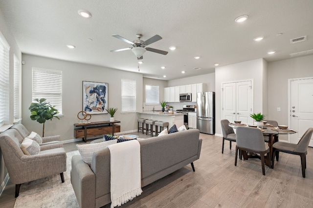 living room featuring recessed lighting, ceiling fan, light wood-type flooring, visible vents, and baseboards
